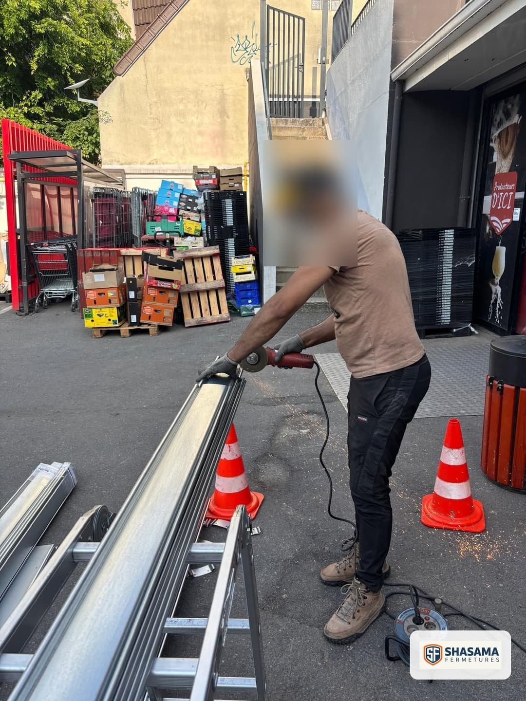 Technicien Shasama Fermetures meulant un profilé de rideau métallique posé au sol, plots de signalisation à proximité