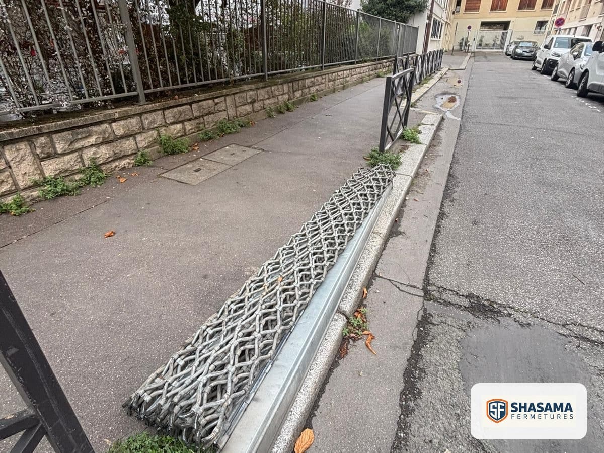 Grille cobra enroulée et profils de rideau métallique neufs posés le long d’un trottoir