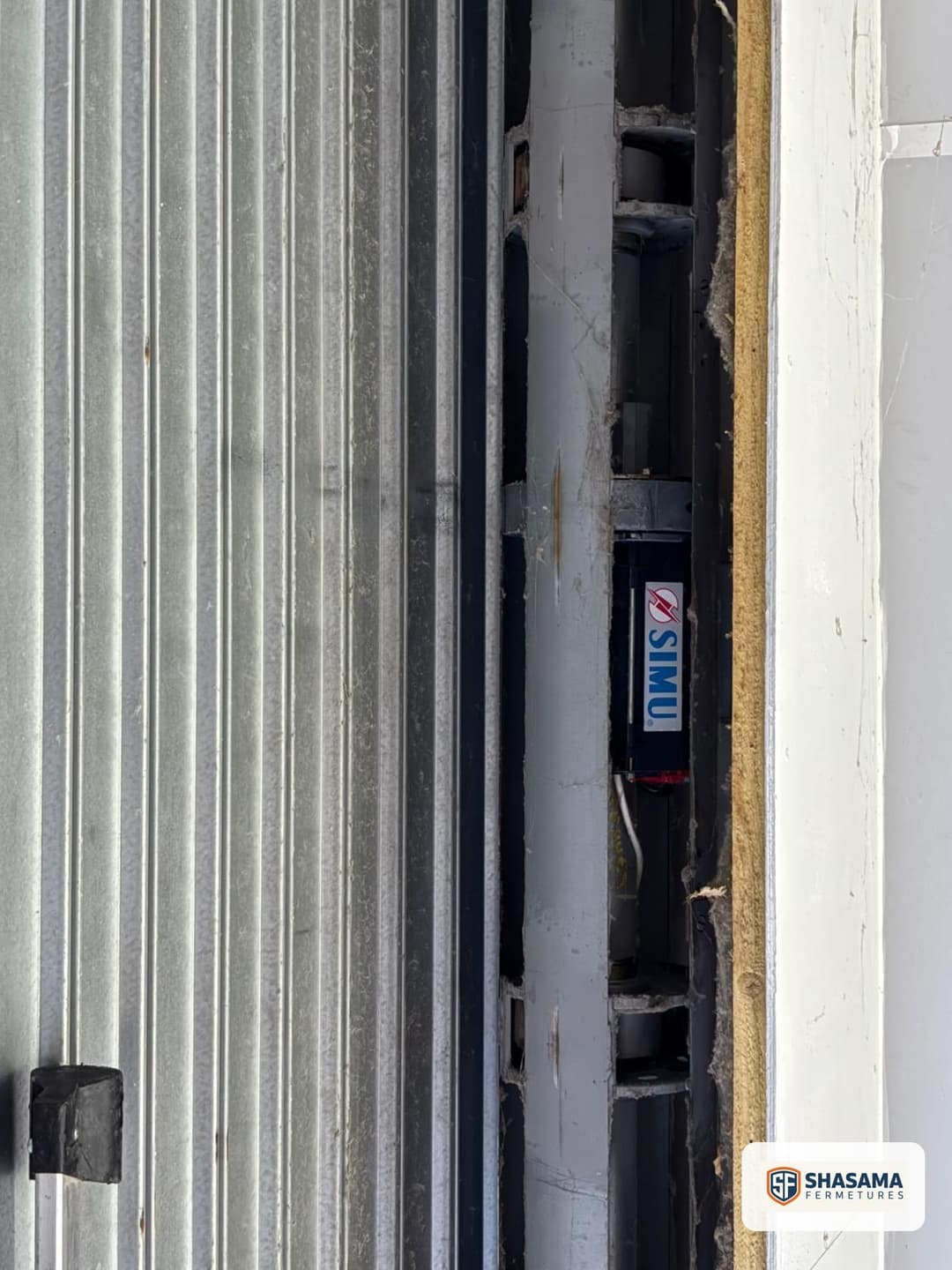 Détail de la coulisse d'un rideau métallique laissant apparaître le tube moteur, étiquette du motoréducteur visible à l'intérieur.