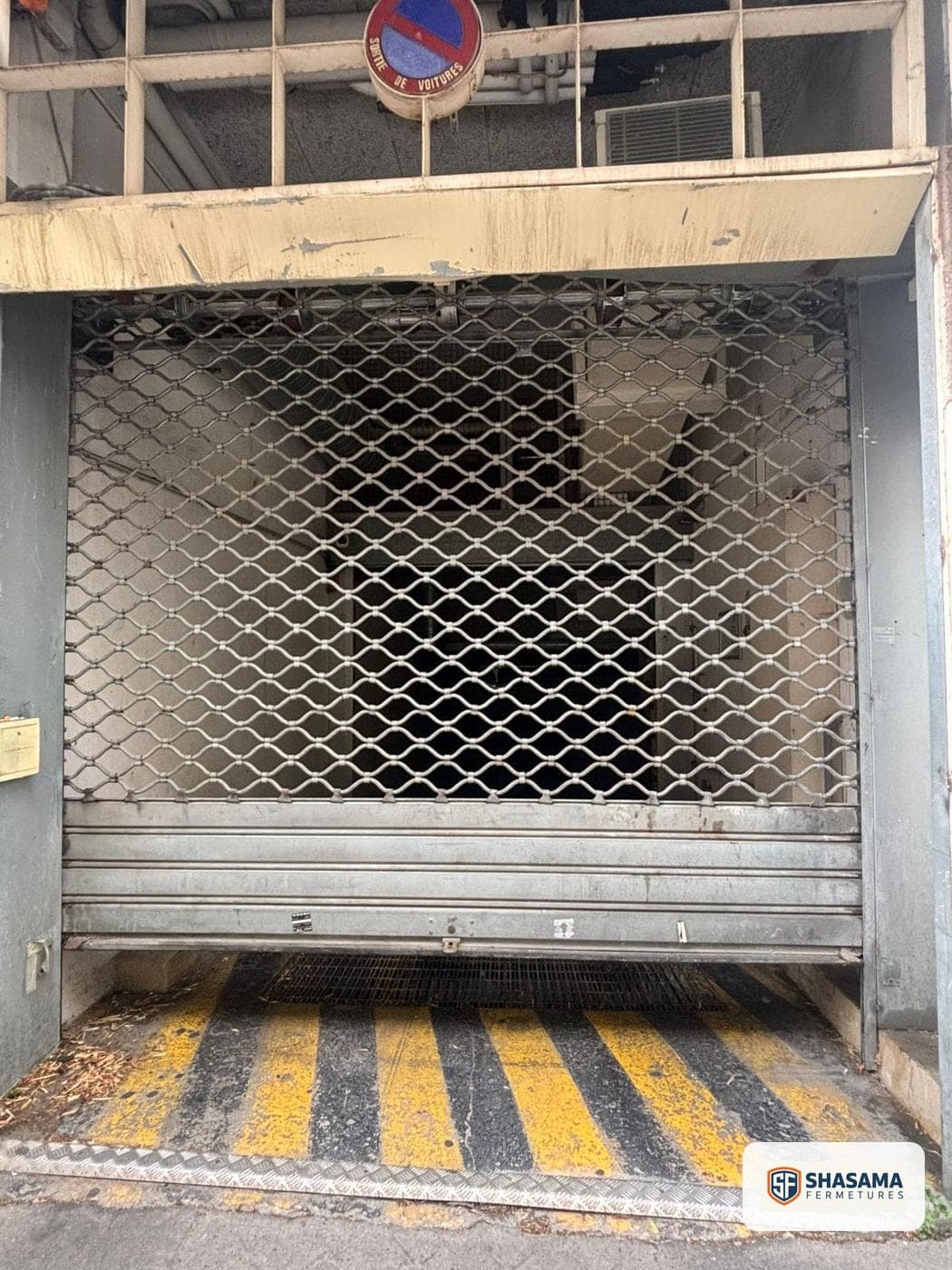 Grille et rideau métallique fermés sous un porche d’accès véhicules