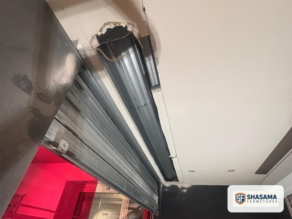 Coulisse du rideau et linteau ouvert en plafond, escabeau au pied de l’ouverture