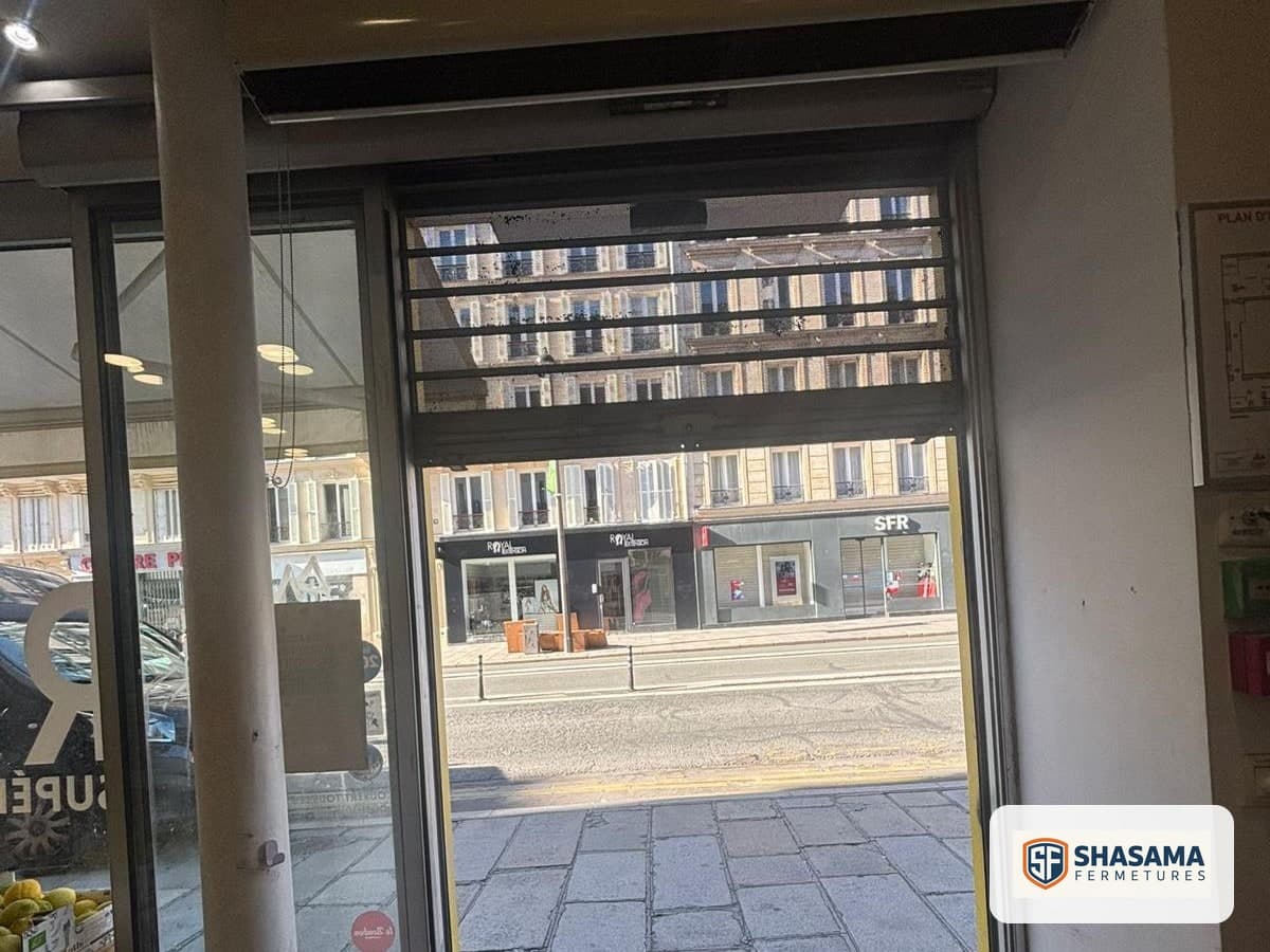 Rideau métallique micro-perforé relevé au-dessus de l’entrée, vu de l’intérieur du commerce