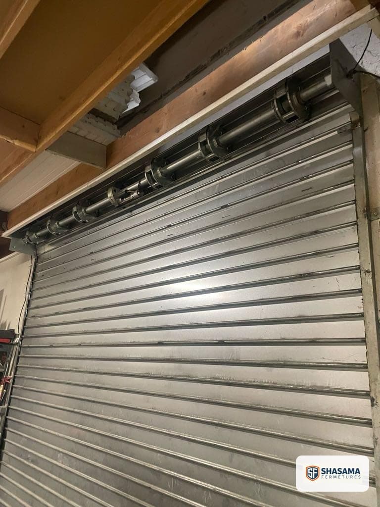 Tablier de rideau métallique et axe moteur visibles dans un coffre en charpente bois