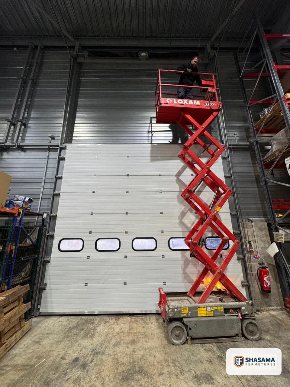 Technician on a work platform adjusting the upper components of a windowed industrial sectional door